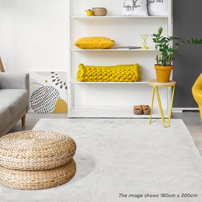 Zubuin Shaggy Plush Fluffy Rectangular Fur Rug - White 90 x 150cm lies elegantly on the floor, complementing the modern decor with its luxurious texture, surrounded by seagrass pouf and minimalist furnishings.