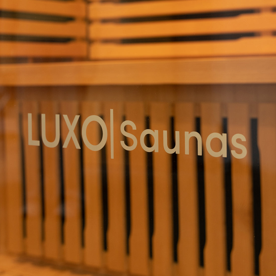 Harlow 2 Person Canadian Hemlock Infrared Home Sauna viewed through branded glass, showcasing warm wooden benches and slats, ideal for indoor relaxation with advanced infrared technology and modern design features.