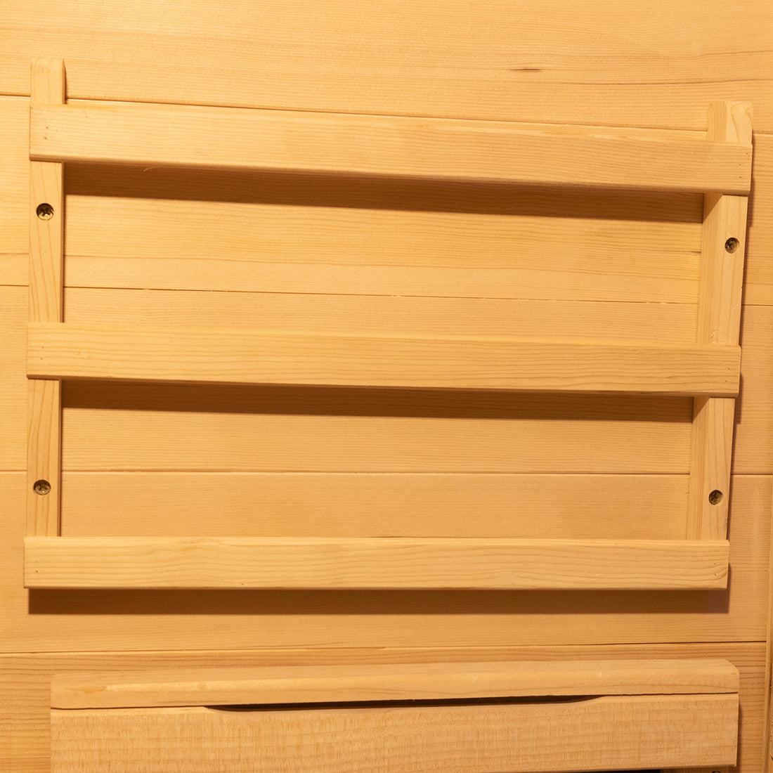Close-up of the Harlow 2 Person Canadian Hemlock Infrared Home Sauna, featuring a wooden rack with vertical supports and horizontal slats, crafted from pale wood matching the wall background.