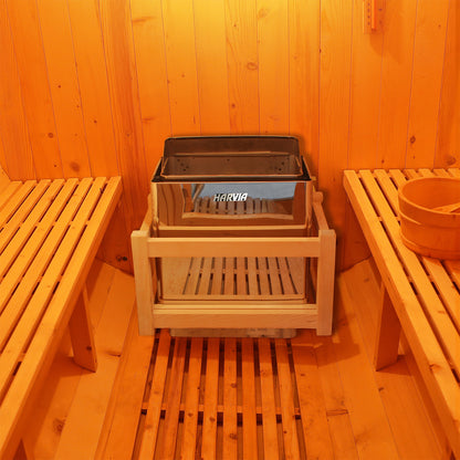 Close-up of the 6kW Harvia Stove Heater for Luola 2 Person Sauna, showcasing its sleek, stainless steel design, positioned beside wooden furniture indoors, emphasizing its durable construction and compact dimensions.
