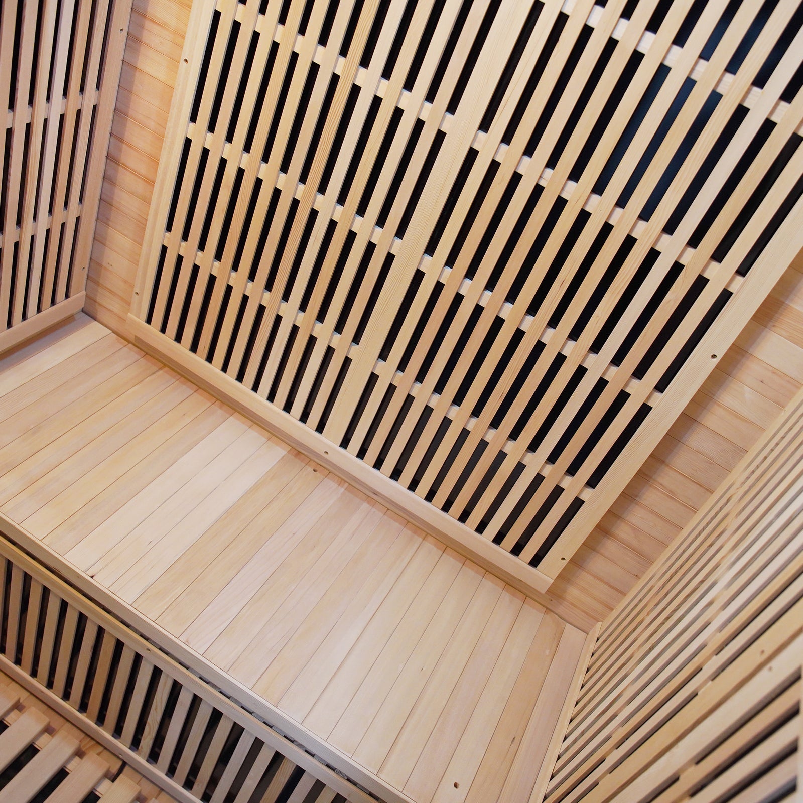 Hirsi 2 Person Carbon Fibre Infrared Indoor Home Sauna featuring light-tone wooden bench seating, slatted wall panels, and visible dark infrared heater elements, offering a spacious, relaxing sauna experience at home.