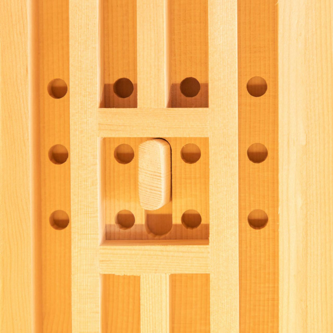 Close-up of the Hoito 4-Person Full Spectrum Infrared Sauna showcasing vertical wooden slats framing a recessed square with drilled holes and a thumb-shaped wooden latch, reflecting its ventilated design.