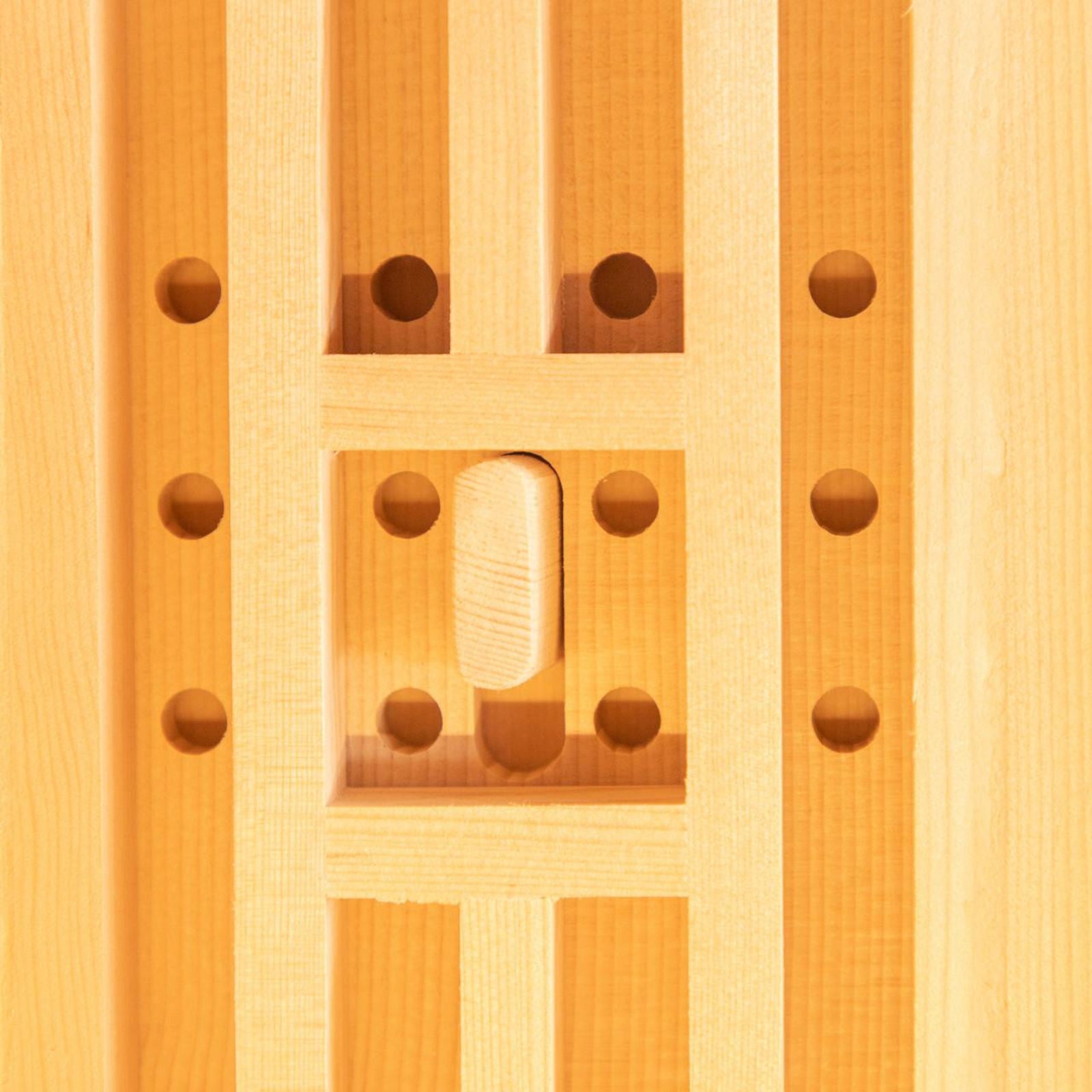 Close-up of the Hoito 4-Person Full Spectrum Infrared Sauna showcasing vertical wooden slats framing a recessed square with drilled holes and a thumb-shaped wooden latch, reflecting its ventilated design.