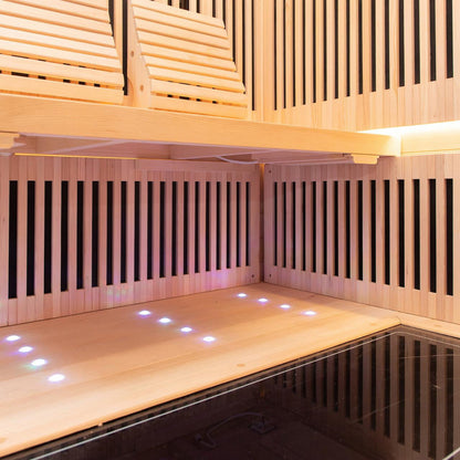 Hoito 4-Person Full Spectrum Infrared Sauna features slatted pine benches, backrests, wooden slats concealing infrared panels, and LED floor lights, offering a spacious, comfortable, and modern spa experience.