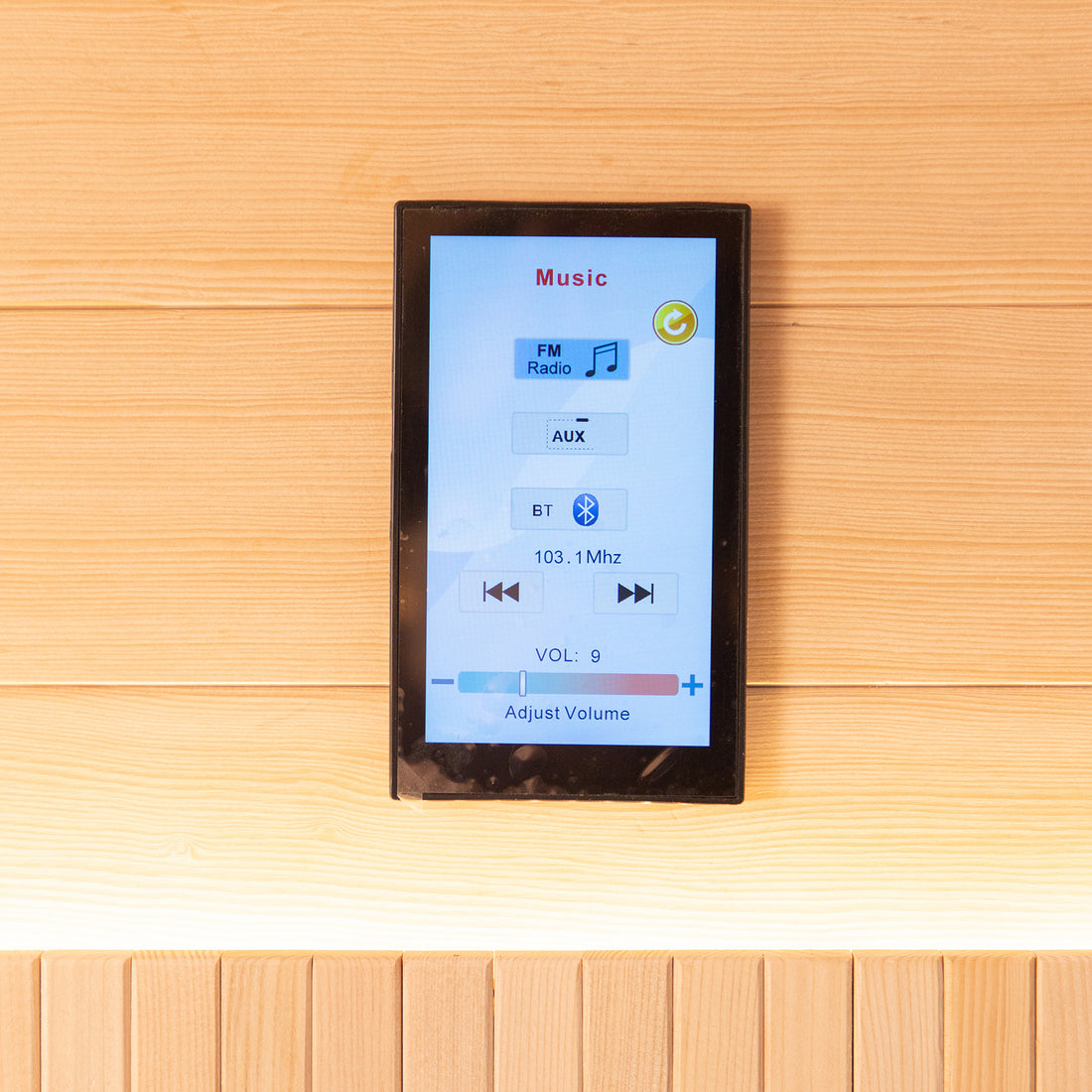 Wall-mounted touchscreen music controller on wood panel, featuring Music header, FM Radio/AUX/Bluetooth modes, tuning at 103.1 MHz, and volume slider for Hoito 4-Person Full Spectrum Infrared Sauna with Glass Floor Heaters.