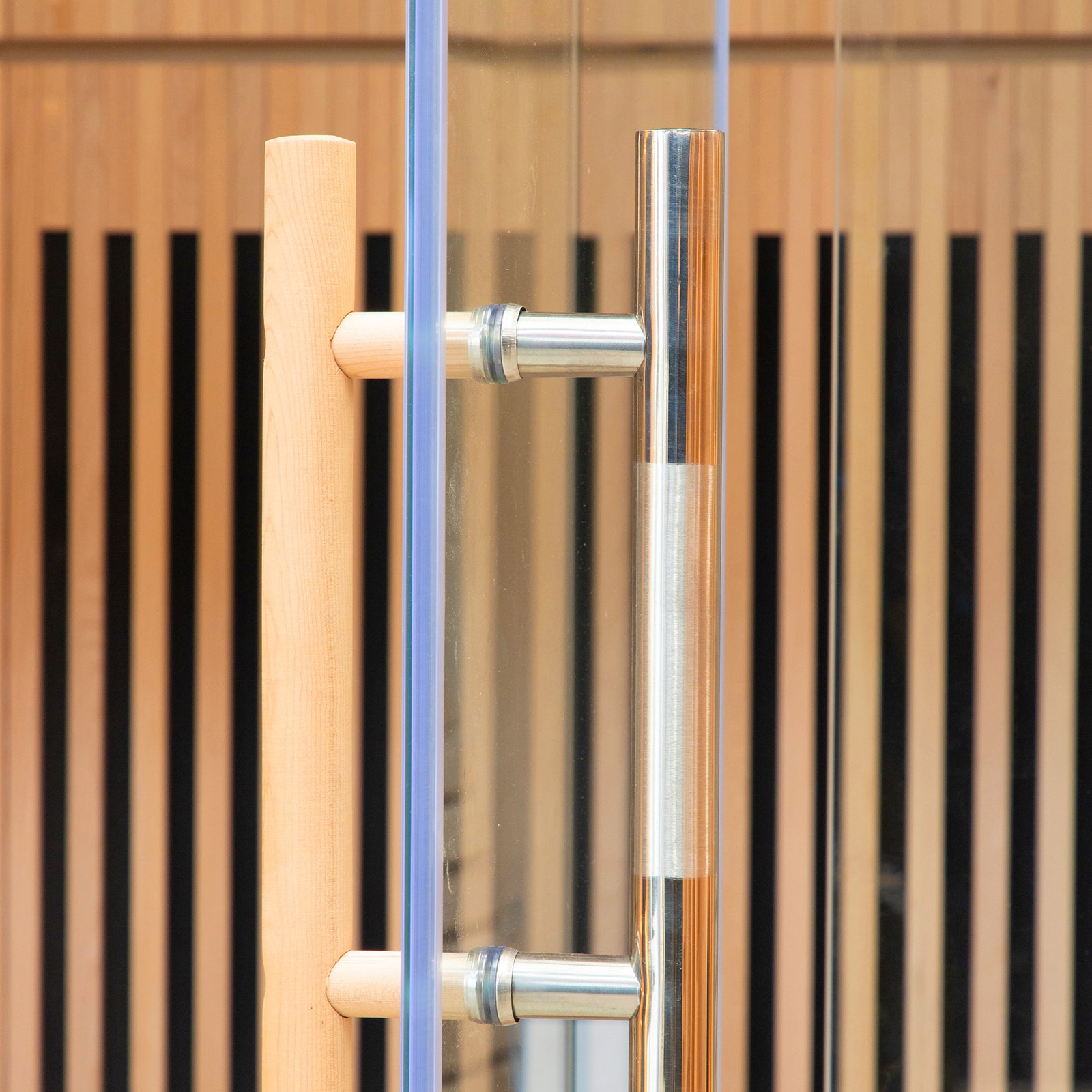 Close-up of the Hoito 4-Person Full Spectrum Infrared Sauna's glass door, featuring a stainless-steel handle and wooden grip, with vertical wood slats in the background, highlighting its modern design.