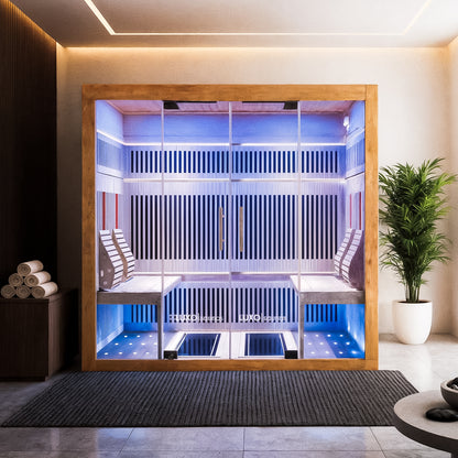 Hoito 4-Person Full Spectrum Infrared Sauna with Floor Heaters in a minimalist spa room, featuring a wood-frame with glass front, blue LED lights, twin benches, and a nearby potted plant.
