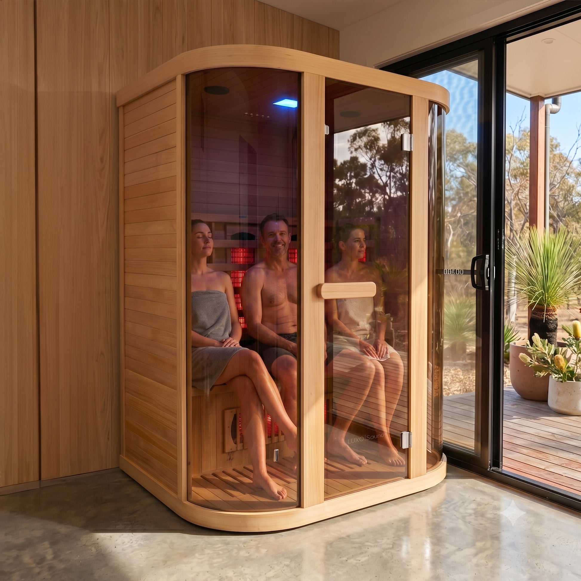 Corner infrared sauna with curved glass front and wooden interior, showing red heating elements and blue chromotherapy light