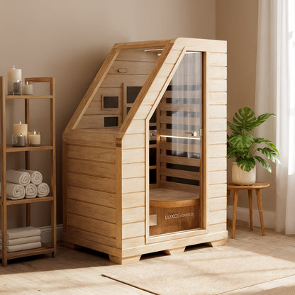 Jarli 1 Person Portable Compact Infrared Indoor Home Sauna, made of Canadian Hemlock, with a tempered glass door, situated between a towel shelf and a potted plant, creating a spa-like ambiance.