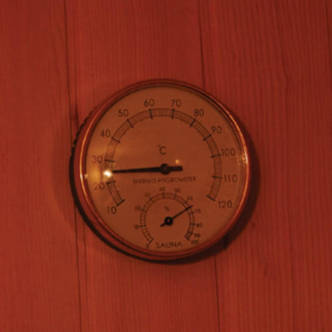 Round analog sauna gauge on a wooden wall for the Kivi 3-Person Traditional Stove Finnish Indoor Home Sauna, showing temperature just under 30°C and humidity, enhancing the sauna experience.