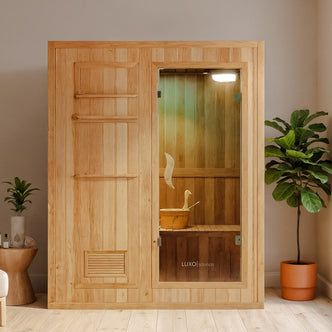 Kivi 3-Person Traditional Stove Finnish Indoor Home Sauna with light wood panels, full-height glass door, interior bench, wooden water bucket, ladle, and softly glowing ceiling light in a minimalist spa setting.