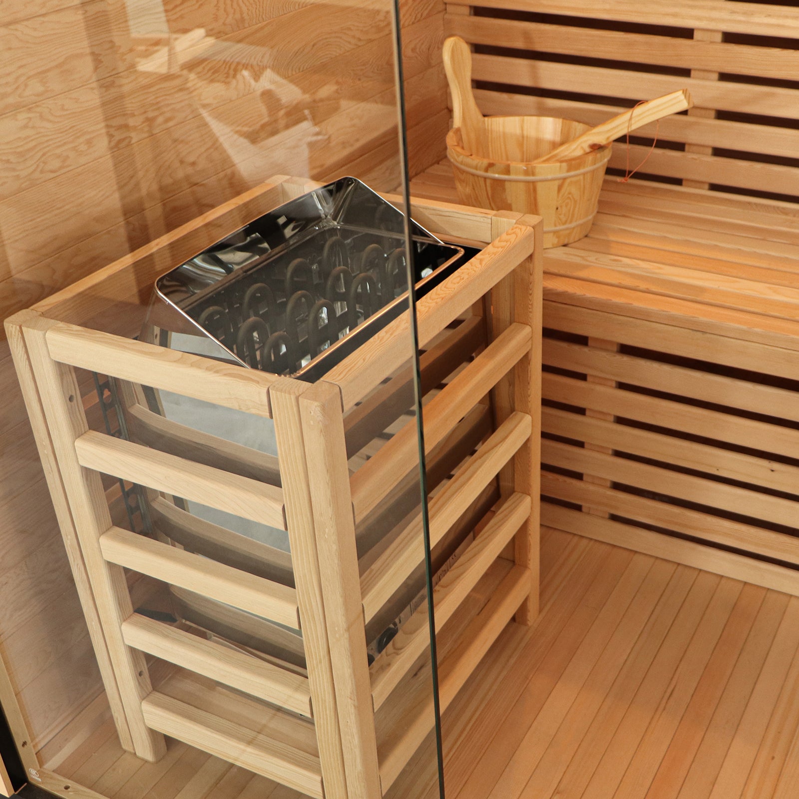 Kivi 4-Person Traditional Finnish Home Sauna interior features a stainless-steel electric heater with safety guard, wooden bench, and bucket with ladle, surrounded by light wood panelling.