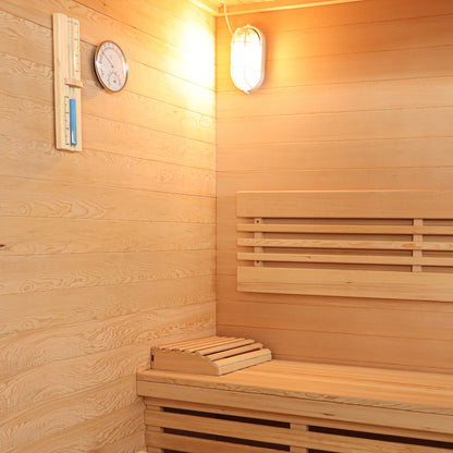 Kivi 4-Person Traditional Finnish Home Sauna interior with light wood paneling, bench seating, headrest, wall-mounted thermometer/hygrometer, and light fixture, showcasing spacious and relaxing sauna environment.