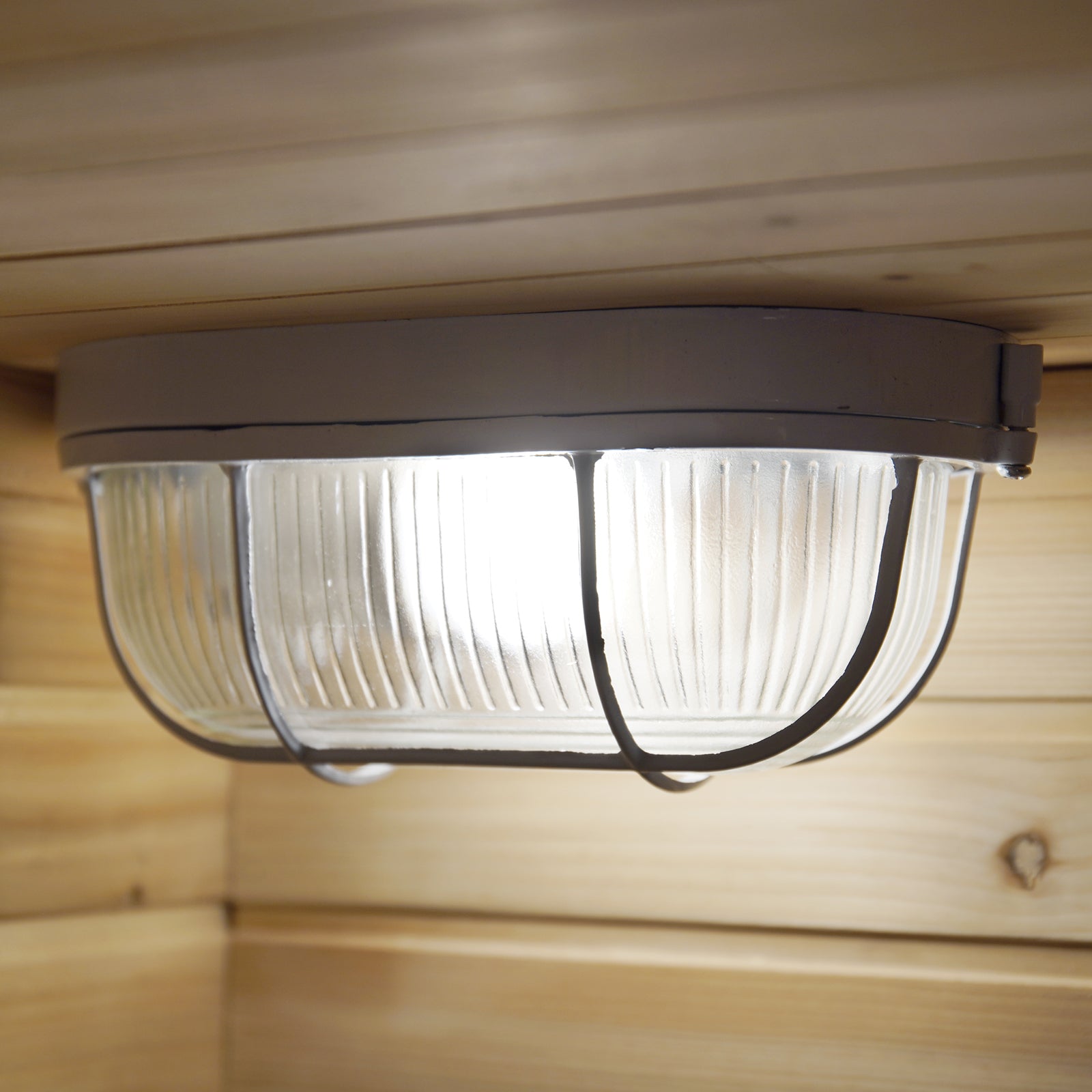 Kivi 4-Person Traditional Outdoor Finnish Home Sauna featuring a ribbed glass diffuser and metal cage ceiling light mounted on wooden paneling, casting an inviting glow for a serene sauna experience.