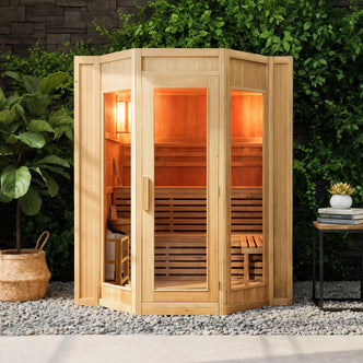 Kivi 6-Person Traditional Finnish Indoor Home Sauna with a wooden multi-paneled cabin, glass-front doors, and warm lighting. Features a wicker basket with white towels and a tall potted plant nearby.