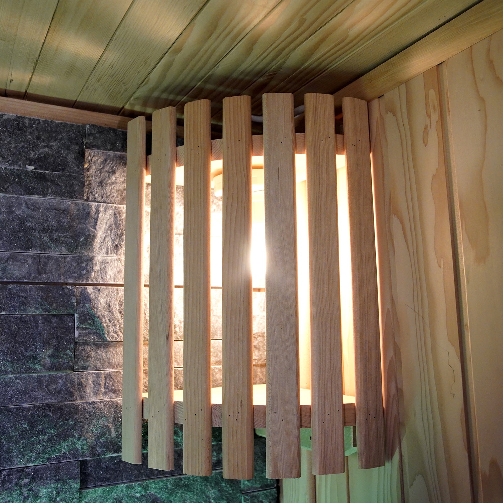 Loyly 3 Person Traditional Finnish Indoor Home Sauna features a wall-mounted light fixture with a wooden cage, set against wood paneling and stone tiles, embodying a spa-style interior.