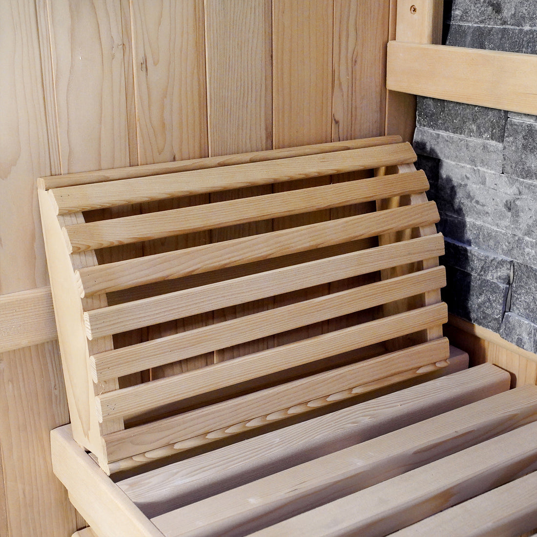 Loyly 3 Person Traditional Finnish Indoor Home Sauna featuring a slatted wooden bench and backrest against a light-wood paneled wall, complemented by dark stone cladding, evoking a serene steam-room ambiance.