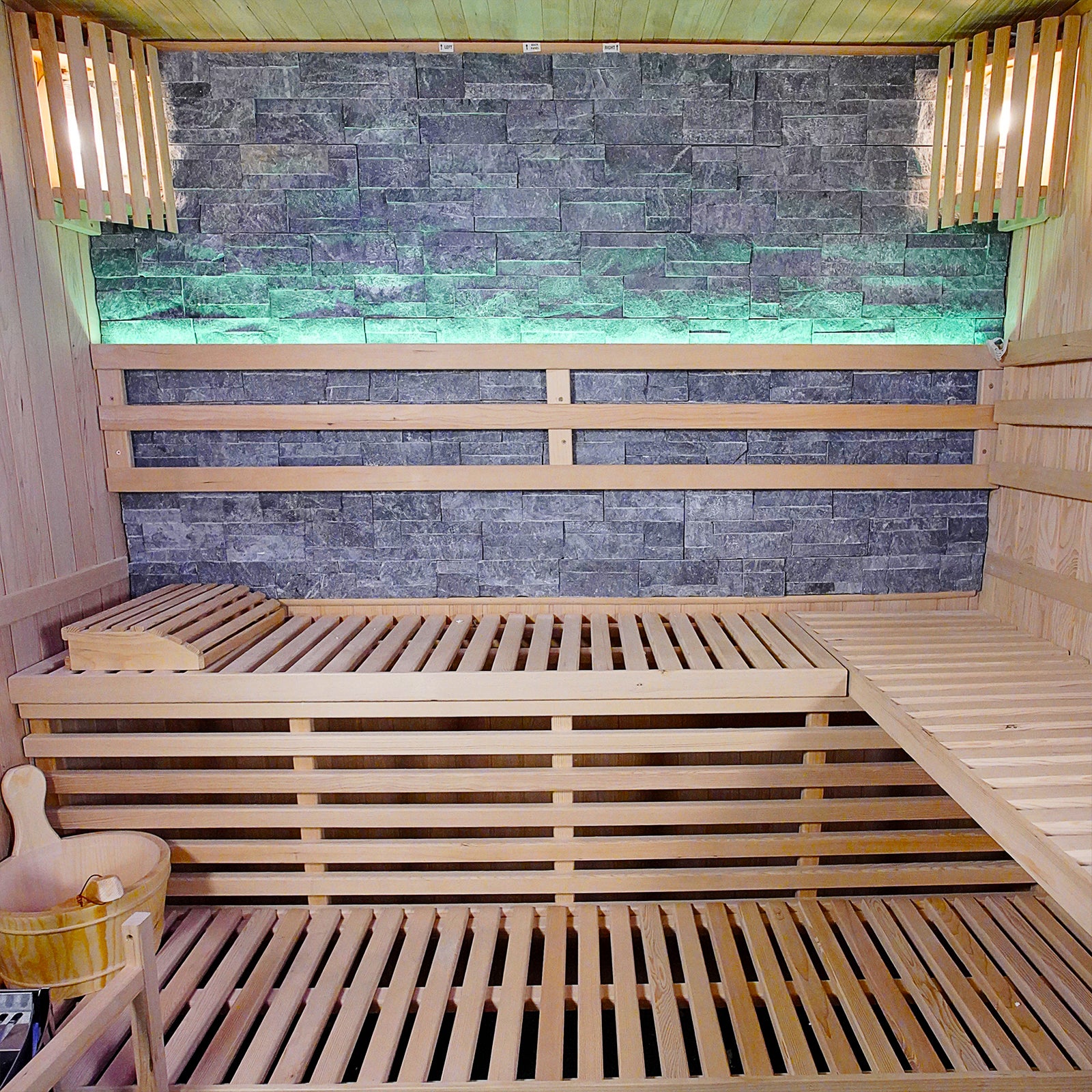 Loyly 3-Person Traditional Finnish Indoor Home Sauna featuring tiered wooden benches, wood-paneled walls, a stone accent wall, and a wooden bucket for creating steam, encapsulating a serene home spa experience.