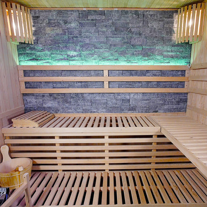 Loyly 3-Person Traditional Finnish Indoor Home Sauna featuring tiered wooden benches, wood-paneled walls, a stone accent wall, and a wooden bucket for creating steam, encapsulating a serene home spa experience.
