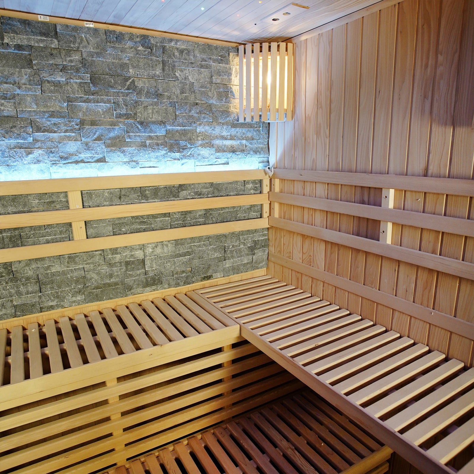 Loyly 3 Person Traditional Finnish Indoor Home Sauna features wood-lined interior, slatted benches, stone accent wall, and wall-mounted light, creating a luxurious and calming sauna experience.