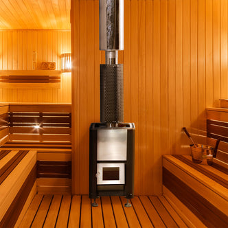 Luola Wood Burning Stove for Luola Outdoor Barrel Saunas centered in a traditional wooden sauna, featuring a metal design with a flue pipe, enhancing the sauna's aromatic and soothing atmosphere.