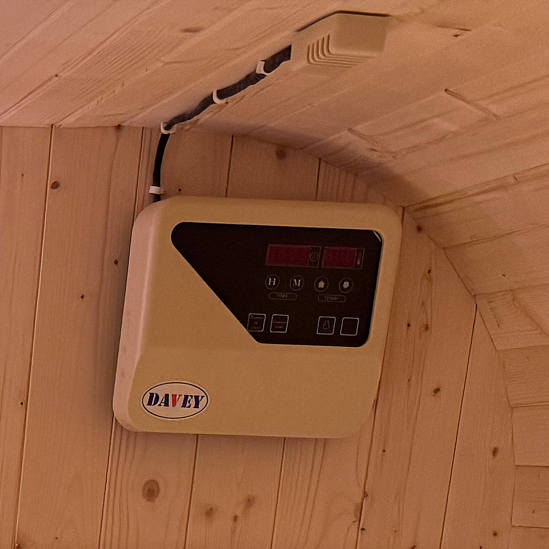 Medika 8 Person Traditional Finnish Outdoor Sauna on a wooden surface, wall-mounted device visible. Sleek design with tempered glass door, showcasing spacious interior for authentic heat therapy and relaxation.