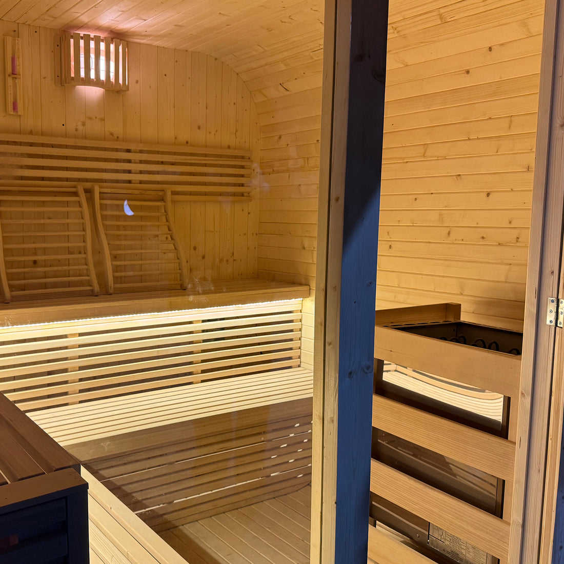 Timber sauna interior with benches, heater and warm lighting