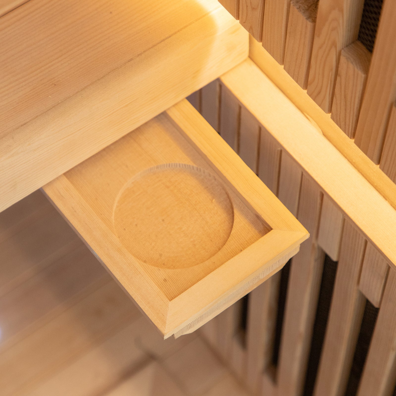 Runko 2 Person Canadian Hemlock Carbon Fibre Infrared Sauna showcased with its smooth, circular wooden exterior, highlighting craftsmanship in woodworking with visible hemlock grain, set on a sturdy wooden shelf.