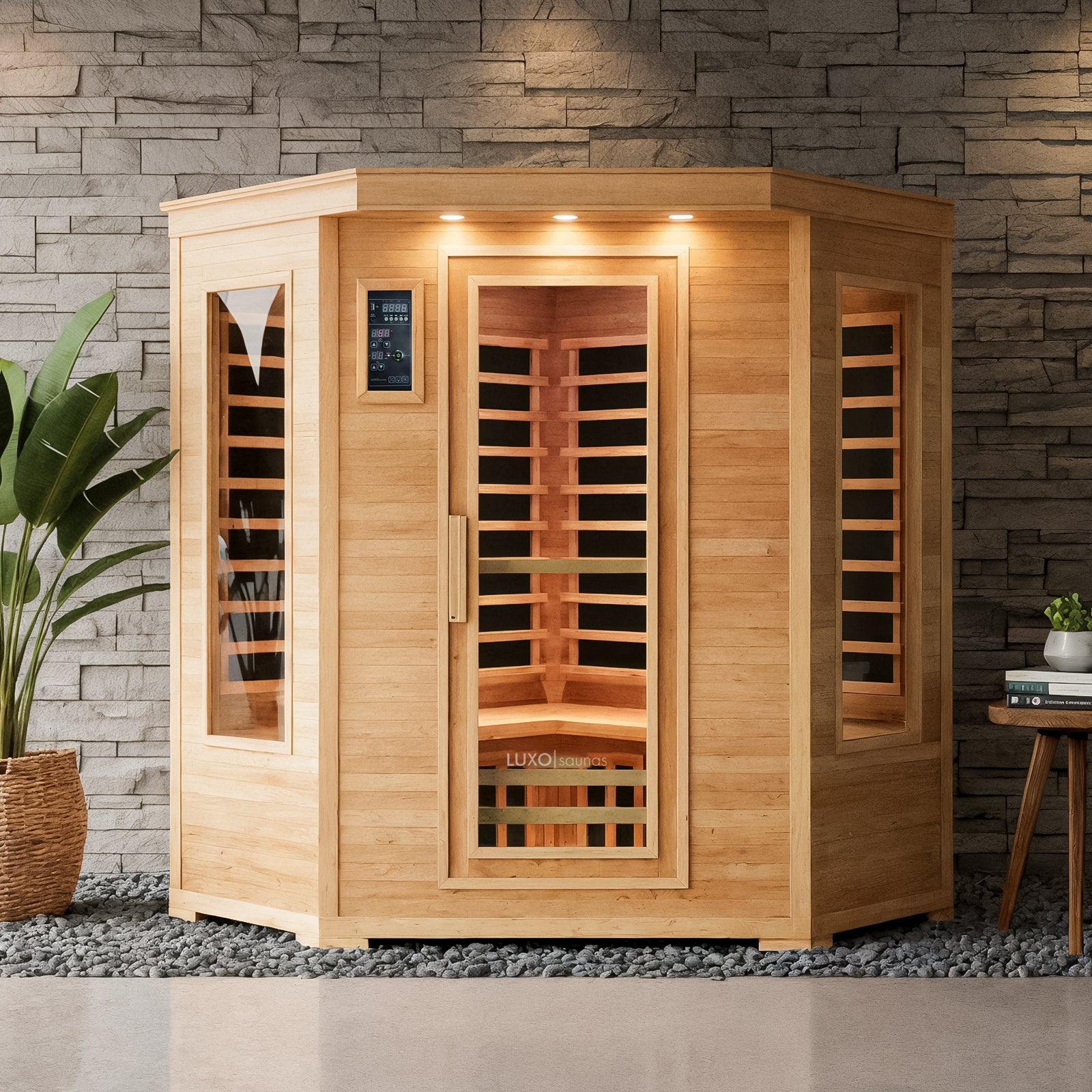 Taavi 4 Person Corner Carbon Fibre Infrared Indoor Sauna with hexagonal shape, glass door, and windows, light wood, recessed lights, and slatted bench, set on pebbles by a stone accent wall.