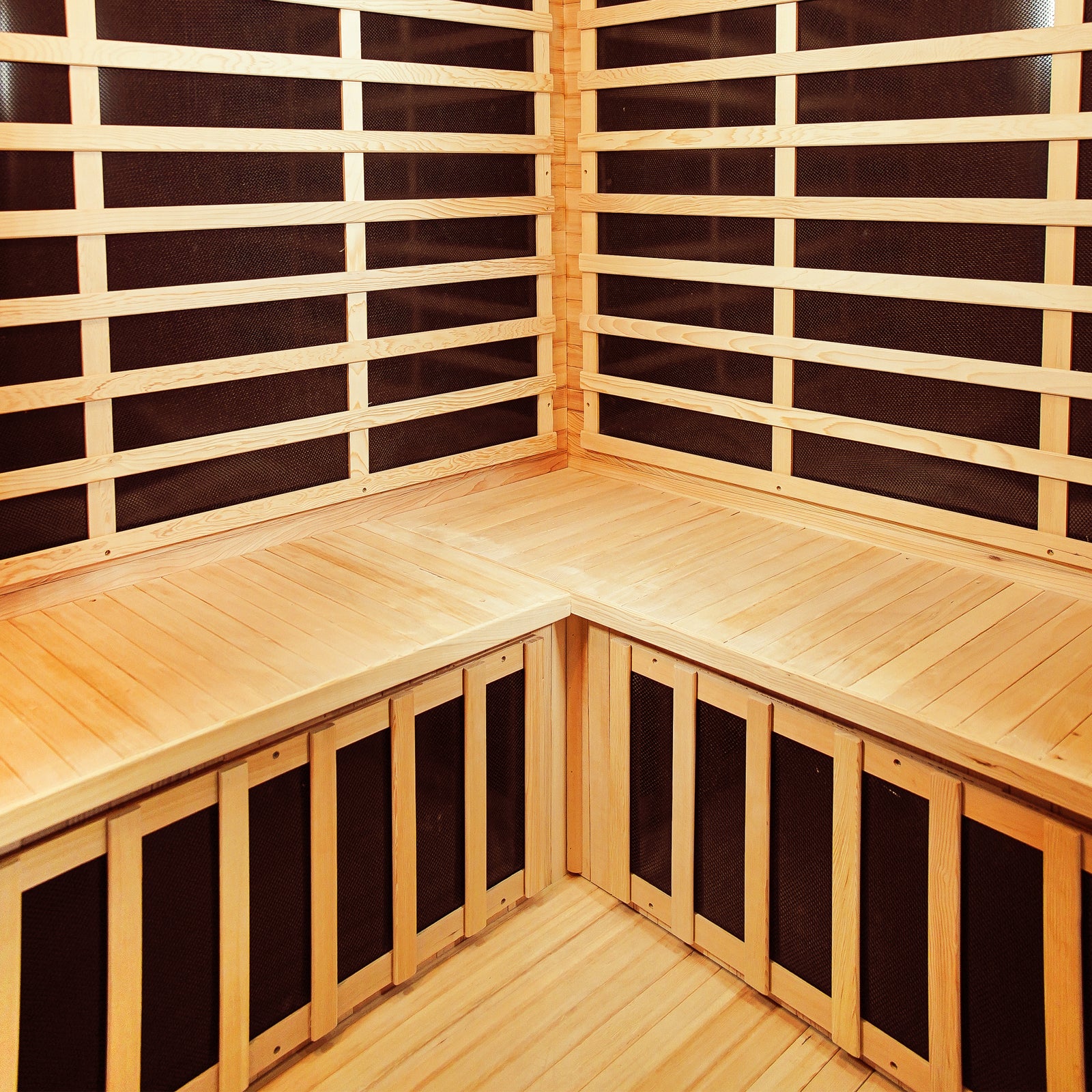 Taavi 4 Person Corner Carbon Fibre Far Infrared Home Sauna interior featuring wooden bench seating, slatted paneling, and visible carbon fibre heating elements, highlighting its spacious design and infrared technology for home relaxation.