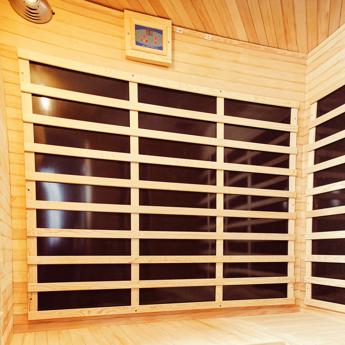Taavi 4 Person Corner Carbon Fibre Far Infrared Home Sauna interior with light wooden paneling, hidden black infrared heating panels, and a digital control unit, showcasing spacious design for home relaxation.