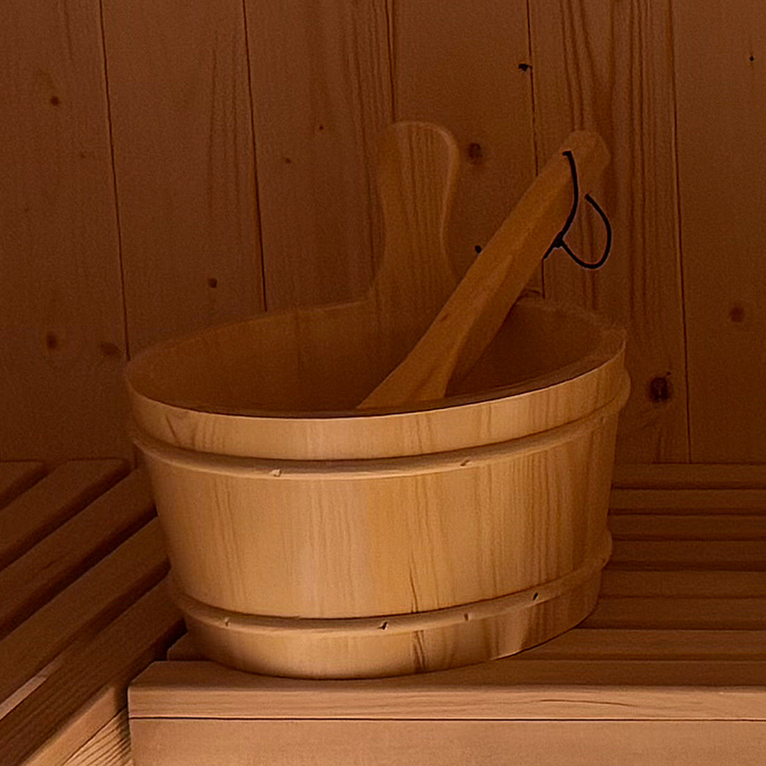 Wooden sauna bucket and ladle on bench, representing the Tarni 2-Person Finnish Outdoor Sauna – Fir Wood, highlighting traditional sauna accessories in a wood-paneled setting for authentic relaxation.