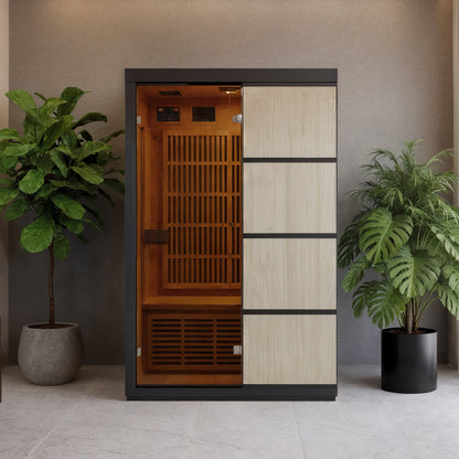 Tumma 2-Person Carbon Fibre Infrared Home Sauna with open side revealing wooden bench, surrounded by light wood panels and potted plants, showcasing its sleek, modern design and craftsmanship.