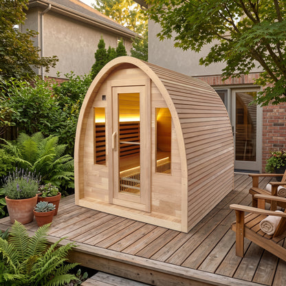 Wooden barrel sauna with glass door and windows on a timber deck, surrounded by ferns and potted plants