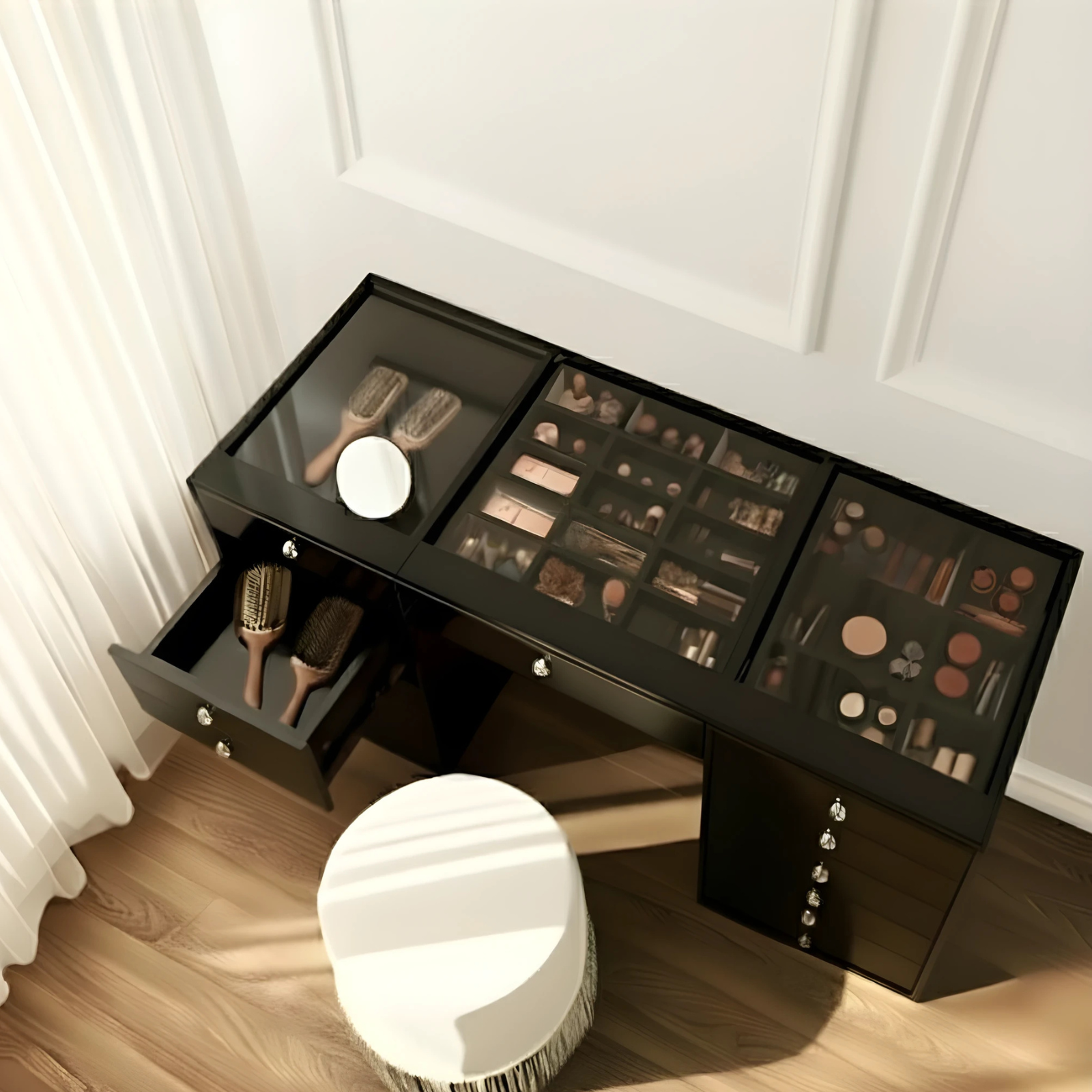 Adeline Glass Top Dressing Table in Black, featuring a sleek glass surface with organized compartments for cosmetics. Includes a partially opened drawer with brushes and a white stool against a panelled wall.