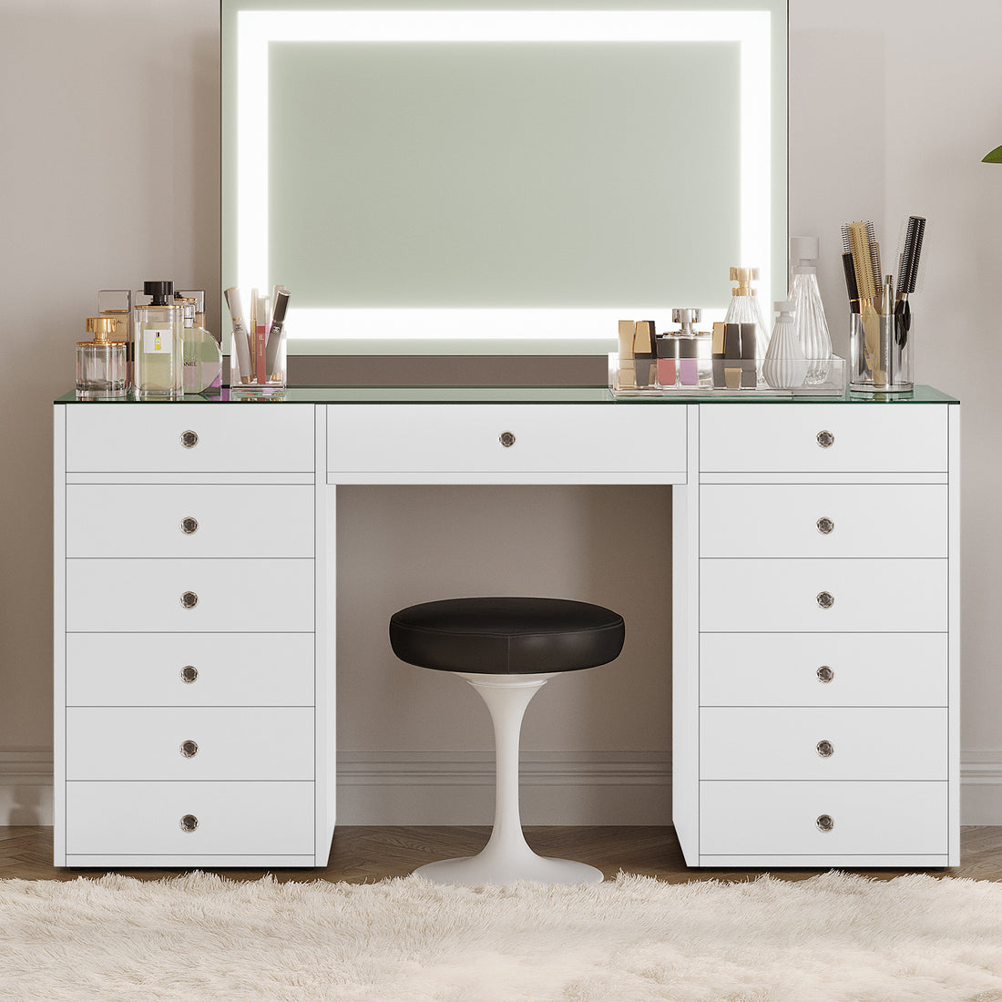 Adeline Glass Top Storage Makeup Dressing Table Desk in White featuring a large LED mirror, multiple drawers, perfume bottles, makeup containers, and a black-cushioned stool on a plush rug.
