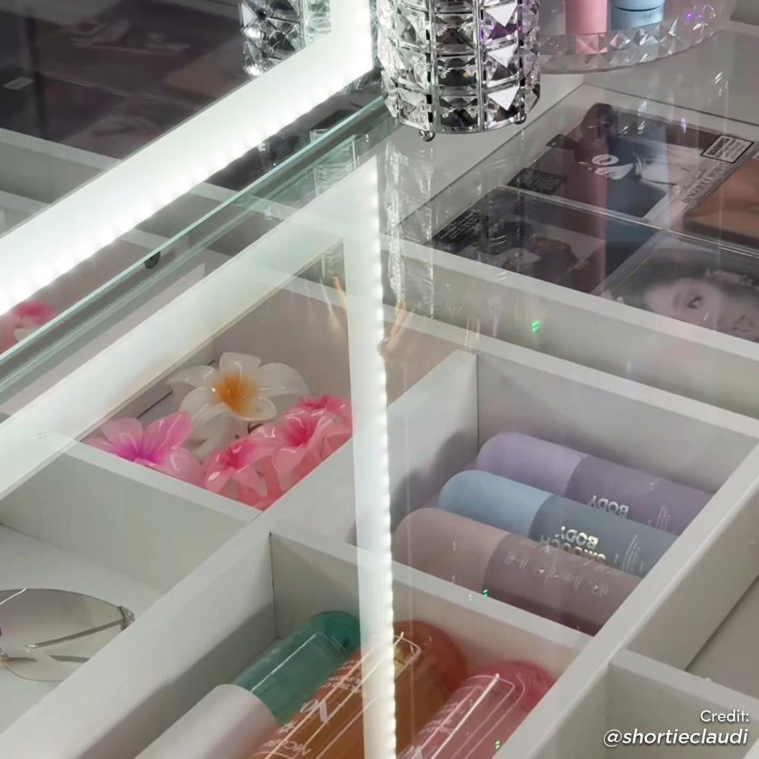 Adeline LED Mirror Storage Dressing Table in White featuring a glass-top with pastel bottles, flower clips, sunglasses in cubbies, and an acrylic holder on top, showcasing modern elegance and organization.