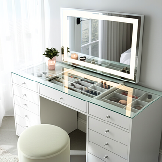 Adeline LED Mirror Storage Dressing Table in White features a glass countertop revealing organized cosmetics. It includes a large LED-lit mirror, multiple drawers, a potted plant, and a round stool.