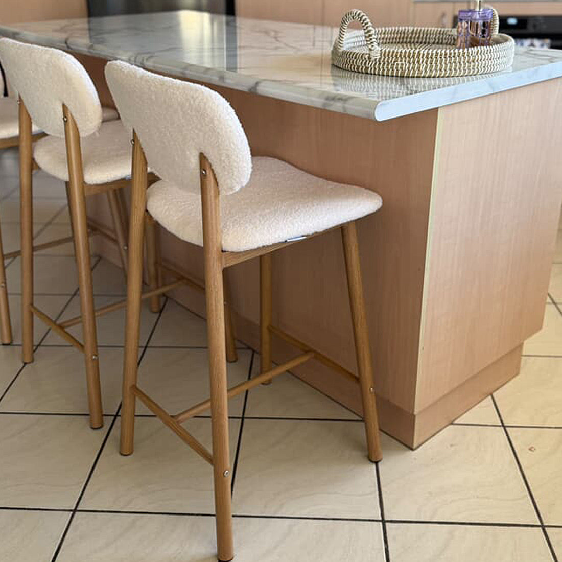 Afrim Boucle High Back Bar Stool Set of 2 in Cream White, featuring plush upholstered seats, light wood legs, and a high backrest, tucked under a marble-look countertop in a modern kitchen setting.