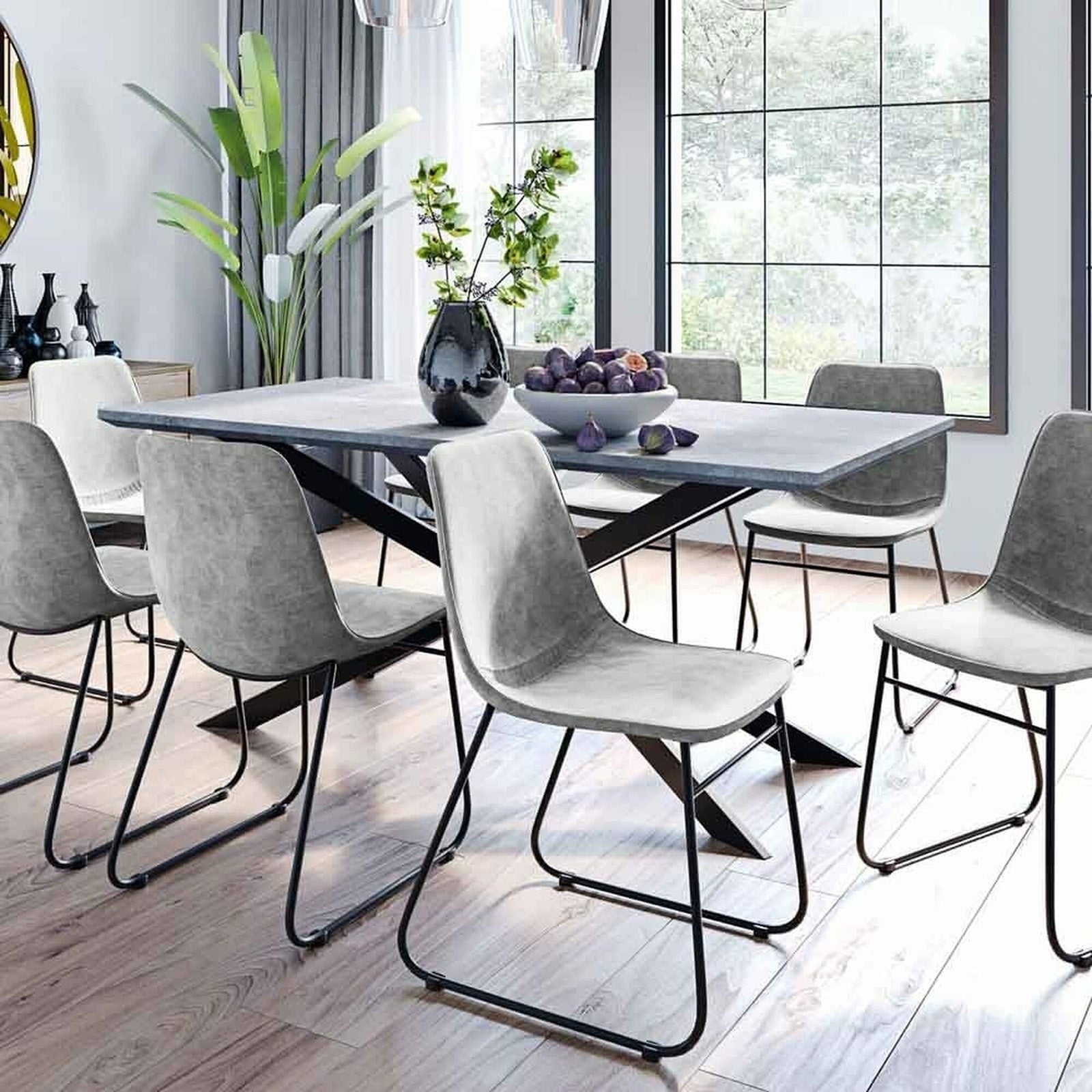 Alfred 180cm 6 Seater Pedestal Dining Table in Concrete, featuring a slim rectangular top and geometric black metal legs, adorned with a dark vase and bowl of purple fruits, set in a bright, modern dining area.