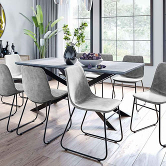 Alfred 180cm 6 Seater Pedestal Dining Table in Concrete, featuring a slim rectangular top and geometric black metal legs, adorned with a dark vase and bowl of purple fruits, set in a bright, modern dining area.