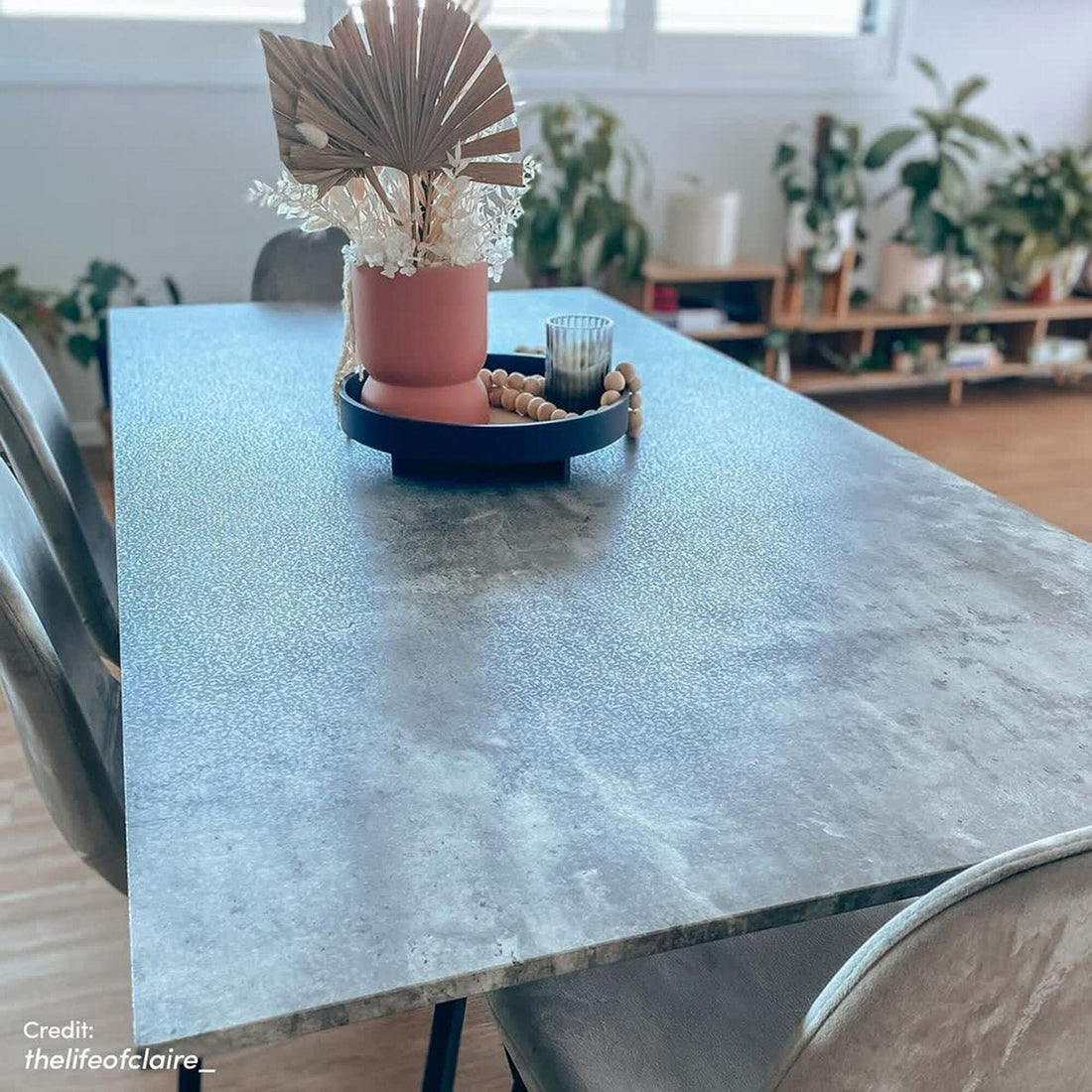 Alfred 180cm 6 Seater Pedestal Dining Table in Concrete with a sleek rectangular surface, adorned with a stylish centerpiece of dried foliage, candle, and beads. Flanked by two upholstered chairs.