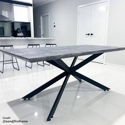 Alfred 180cm 6 Seater Pedestal Dining Table in Concrete, featuring a thick rectangular tabletop with a grey concrete-look finish and a black metal spider-style base, set in a modern white room.