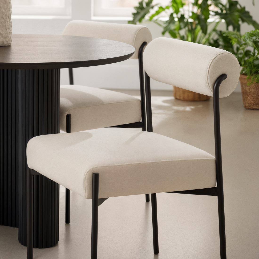 Alona Modern Velvet Dining Chair Set of 2 in Cream White features cream-colored velvet upholstery with curved tubular backrests and slim black metal legs, placed in a minimalist dining nook setting.