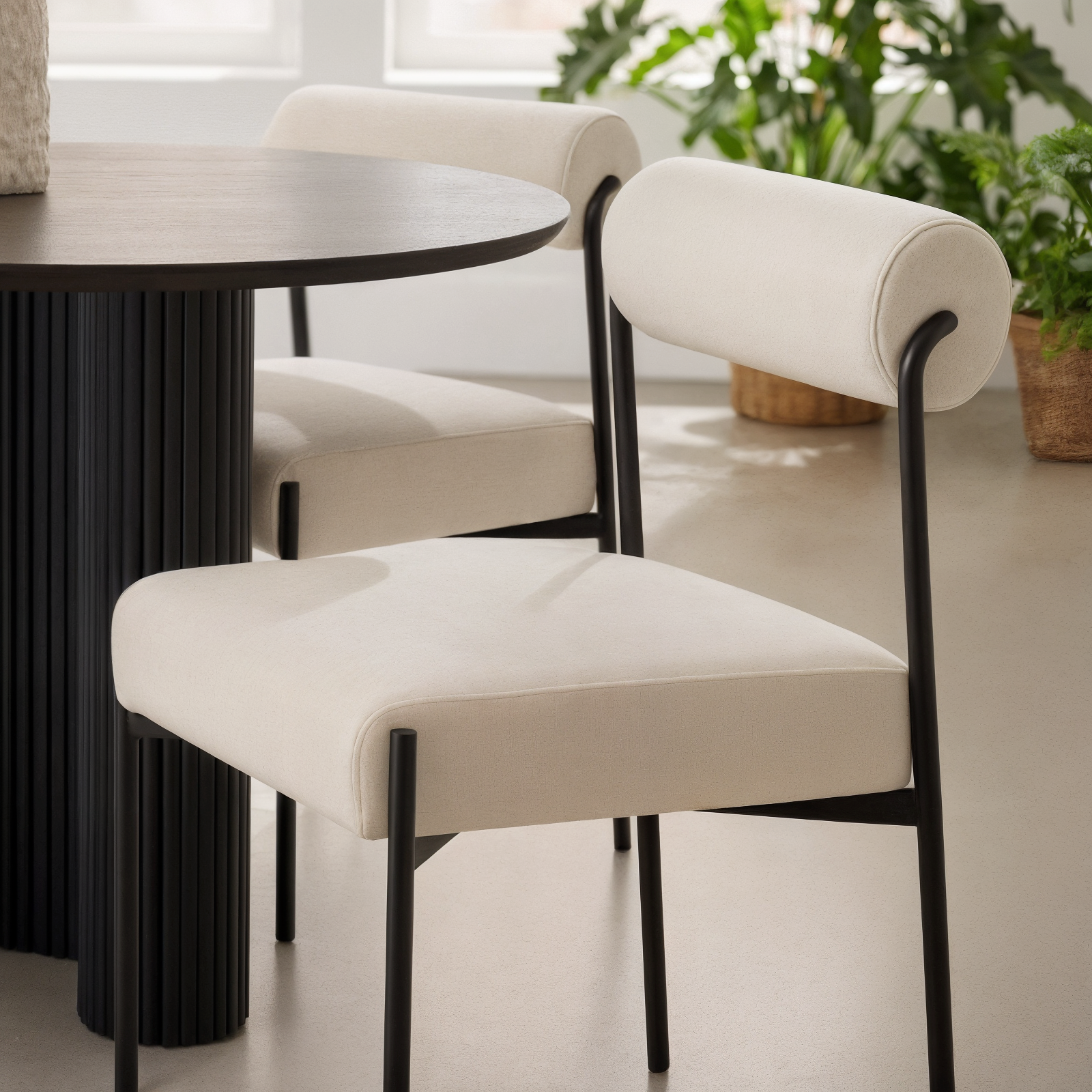 Alona Modern Velvet Dining Chair Set of 2 in Cream White features cream-colored velvet upholstery with curved tubular backrests and slim black metal legs, placed in a minimalist dining nook setting.