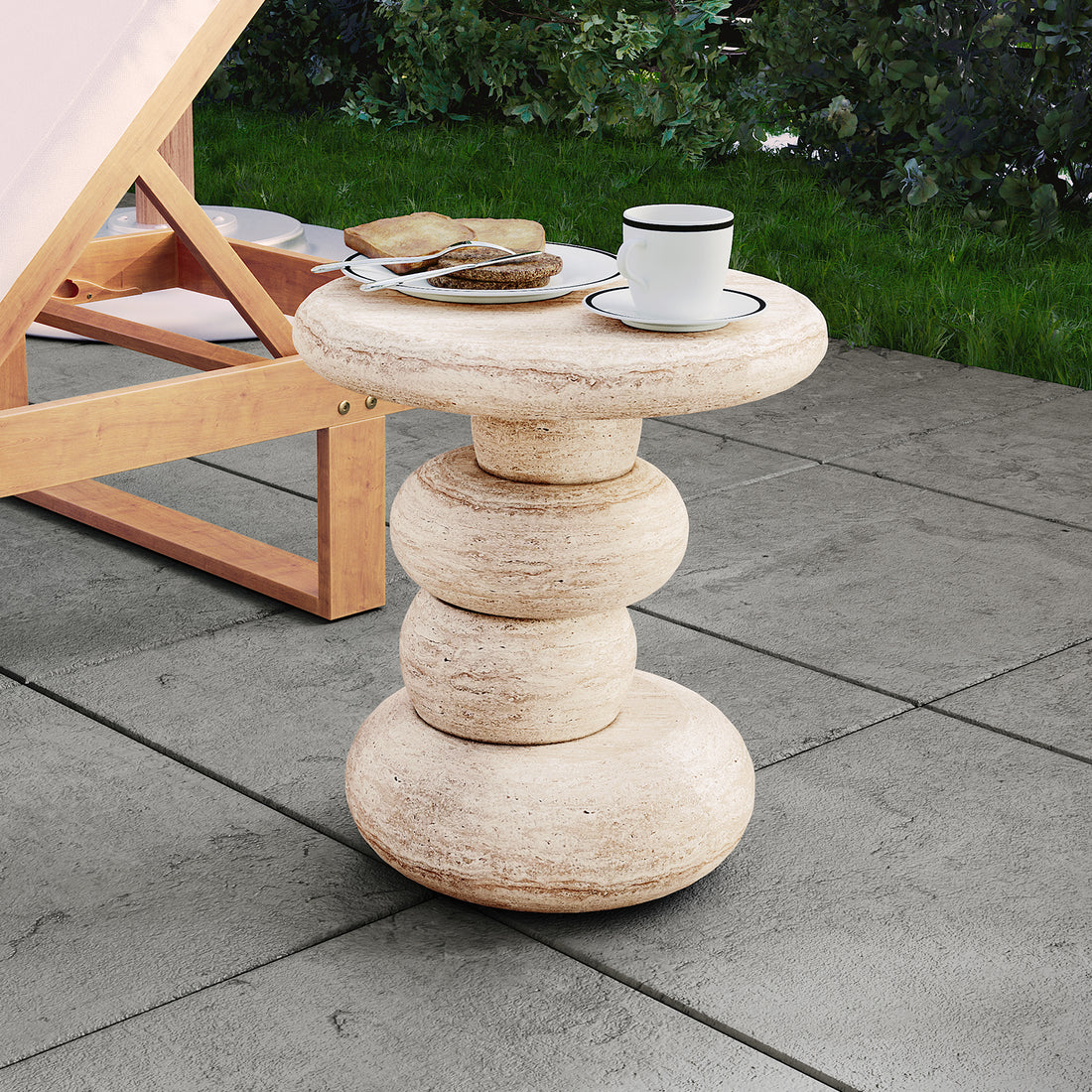 Amalee 40cm Round Concrete Side Table in Travertine, featuring a sculptural base of stacked stone-like discs, topped with a teacup on a saucer, set on a patio with lounge chair nearby.