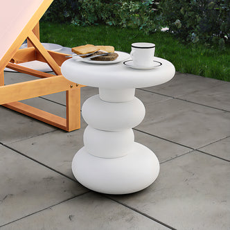 Amalee 40cm Round Indoor/Outdoor Concrete Side Table White on a patio with a white cup, saucer, and toast plate. Adjacent to a wooden-framed lounge chair, set against grass and shrubbery backdrop.