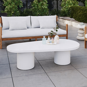 Amarosa Curved Indoor/Outdoor Concrete Coffee Table White with a sculptural design, featuring two cylindrical pedestal legs, topped with decorative vases and foliage, set in a modern outdoor seating area.