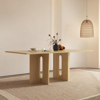 Amora 200cm Dining Table - Natural with sculptural “A-style” legs, oak veneer finish, topped with decorative items like a ceramic bowl, magazine, vase, and fruit dish, beneath a woven lamp.