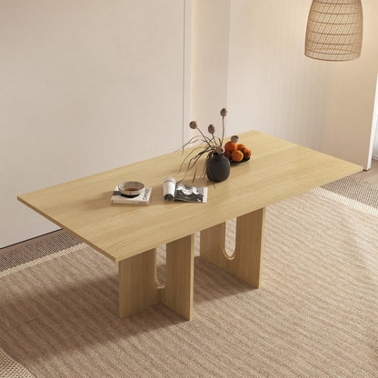 Amora 200cm Dining Table - Natural, featuring a light-wood top and sculptural legs with U-shaped cutouts, adorned with reading materials, a black vase, and a bowl of oranges.